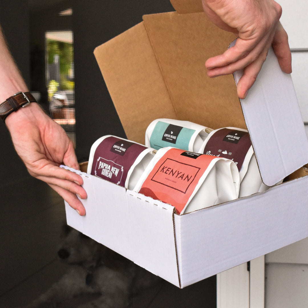 coffee beans packed in four bags into a slightly opened box and being hand delivered to a persons door.