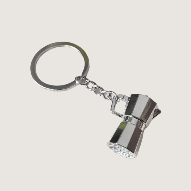 A tiny silver Moka pot keychain featuring a classic Italian espresso maker shape, ideal for coffee enthusiasts.